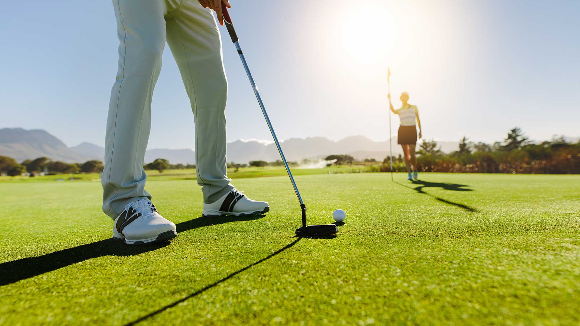 Golfer beim einlochen und Frau hält Stange